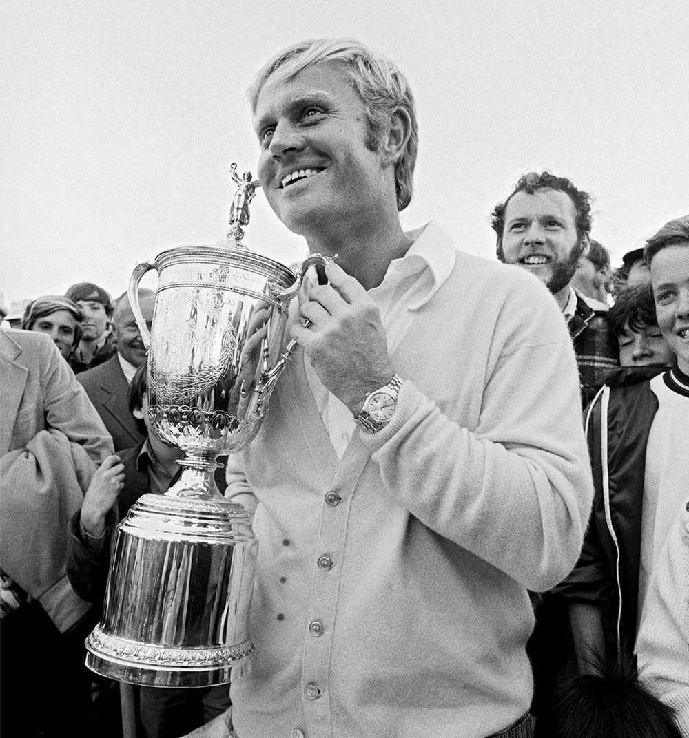 Jack holding the US Open trophy in a white cardigan, the gold numeral 18 overlaid.