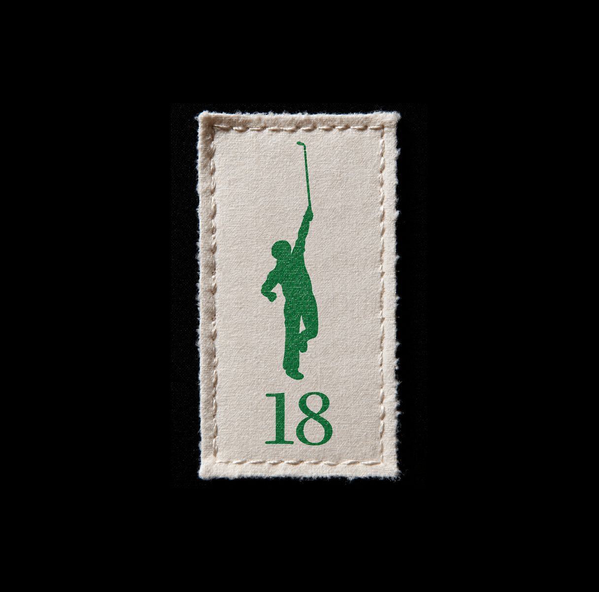 A small woven cream label on black, carrying the green golfer silhouette above the numeral 18.