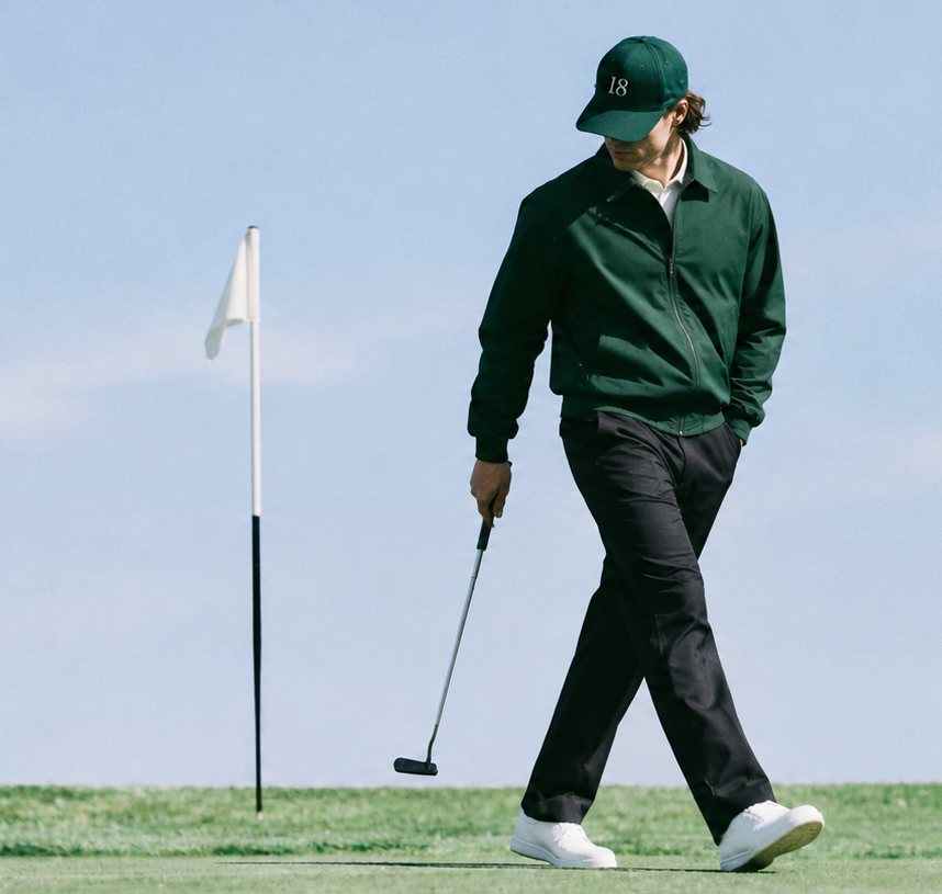 The 18 cap on the course, worn with a green jacket, putter in hand beside the flagstick.