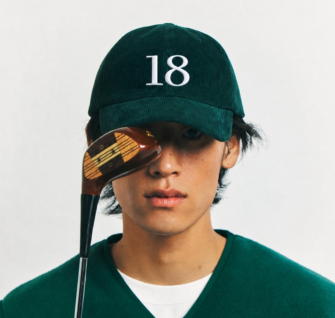 Studio portrait of the green corduroy 18 cap, a wooden club held across the eyes.