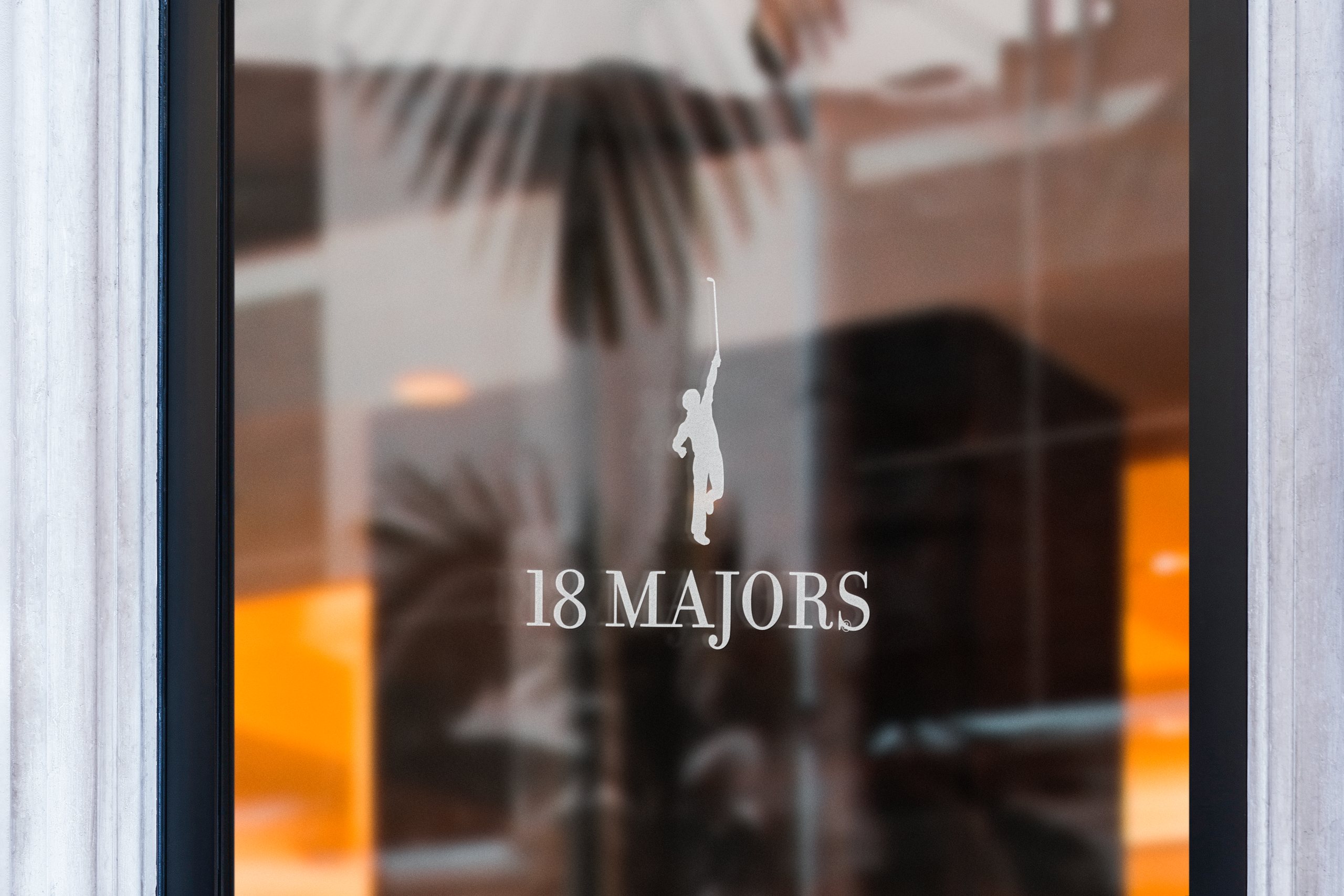 The flagship window at dusk, the golfer silhouette and 18 Majors name etched across black glass.
